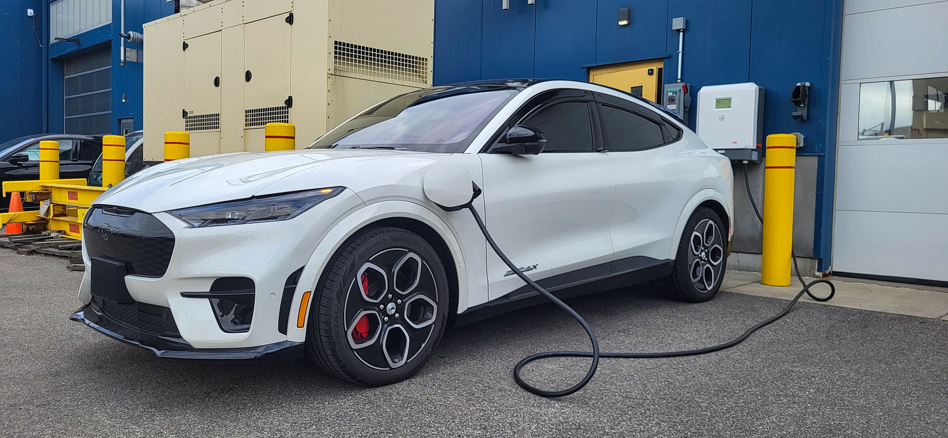 A white Mustang Mach-E® SUV is plugged into a charger.  